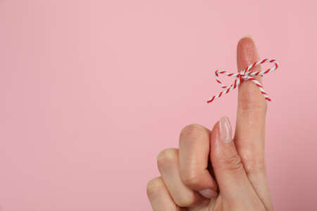 Woman showing index finger with tied bow as reminder on pink background, closeup. Space for text