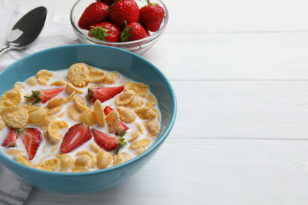 Bowl of tasty crispy corn flakes with milk and strawberries on white wooden table. Space for text