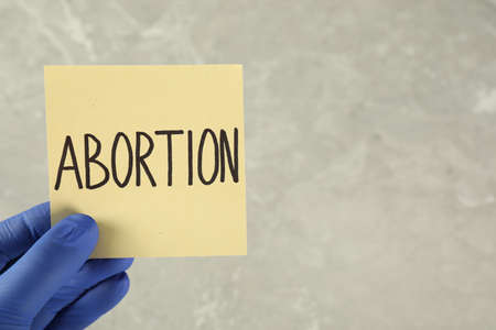 Doctor holding paper card with word ABORTION on light gray background, closeup. Space for textの写真素材
