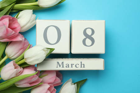 Wooden block calendar with date 8th of March and tulips on light blue background, flat lay....