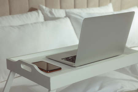 White tray with modern laptop and smartphone on bed indoors