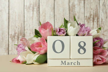 Block calendar with date 8th of March and tulips on table against wooden background. International...