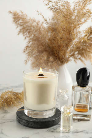 Composition with burning soy candle on white marble table