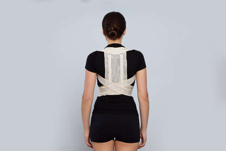 Woman with orthopedic corset on gray background, back view