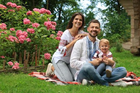 Happy family in Ukrainian national clothes on green grass outdoors