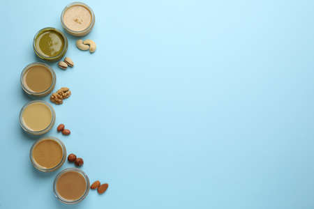 Different types of delicious nut butters and ingredients on light blue background, flat lay. Space...