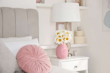 Bouquet of beautiful daisy flowers and lamp on nightstand in bedroomの写真素材