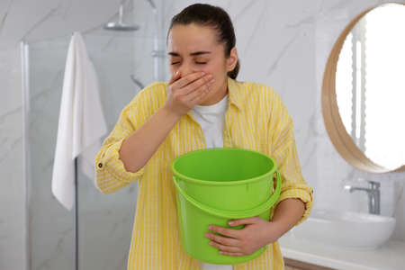 Young woman with bucket suffering from nausea in bathroom. food poisoning