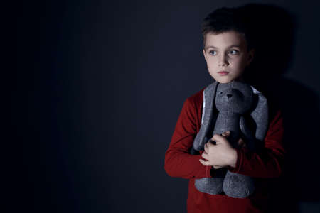 Sad little boy with toy near black wall, space for text. domestic violence concept