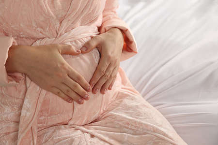 Pregnant woman in bathrobe on bed, closeupの写真素材