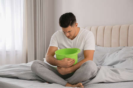 Man with bucket suffering from nausea on bed at home. food poisoningの写真素材