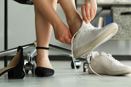 Woman taking off uncomfortable shoes and putting on sneakers in office, closeupの写真素材