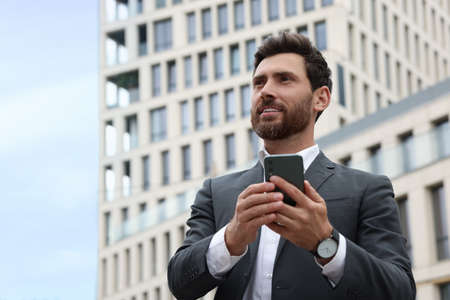 Handsome businessman with smartphone near buildings, space for textの写真素材