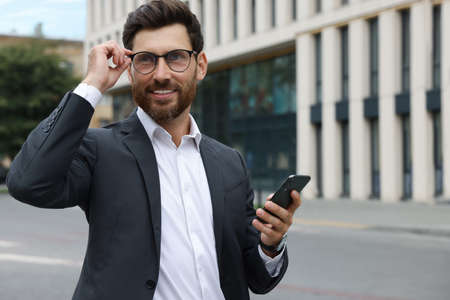 Handsome businessman with smartphone on city street, space for textの写真素材