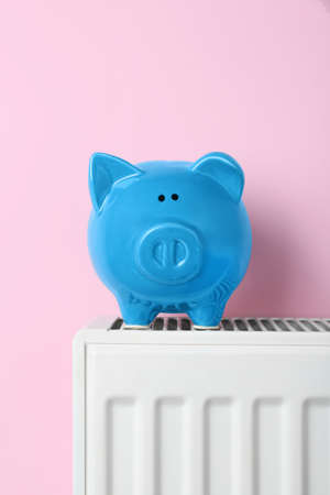 Piggy bank on heating radiator against pink background