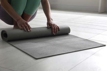 Woman rolling her mat on floor in yoga studio, closeup