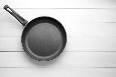 New non-stick frying pan on white wooden table, top view. Space for textの写真素材