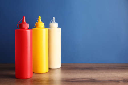 Ketchup, mustard and mayonnaise in squeeze bottles on wooden table against blue background, space...