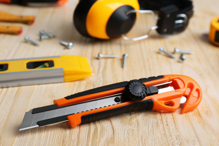 Utility knife and different tools on wooden table, closeup