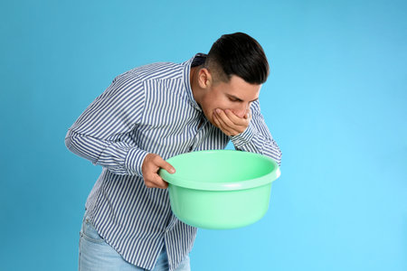 Man with basin suffering from nausea on light blue background. food poisoningの写真素材