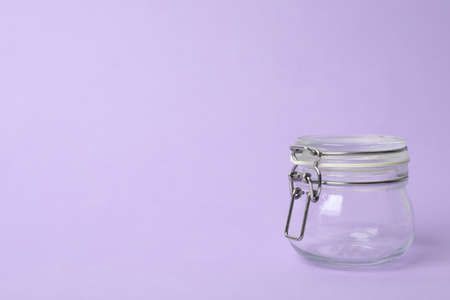 Closed empty glass jar on lilac background, space for textの写真素材