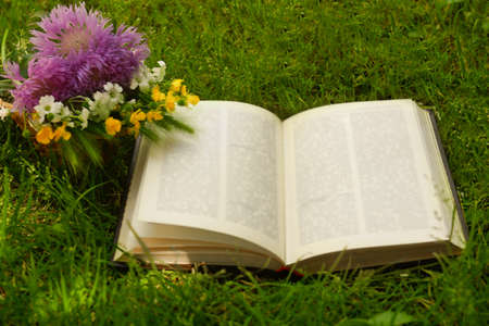 Open book and beautiful wildflowers on green grass outdoorsの写真素材