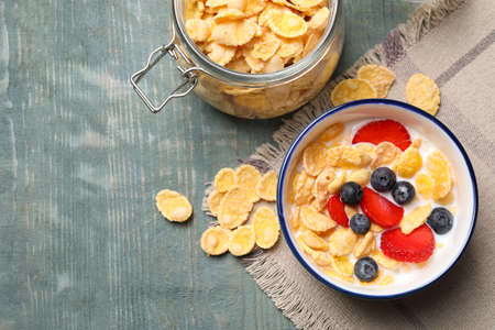 Delicious crispy cornflakes with milk and fresh berries on light blue wooden table, flat lay. Space...