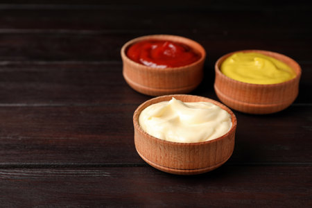 Ketchup, mustard and mayonnaise in bowls on wooden table, space for textの写真素材