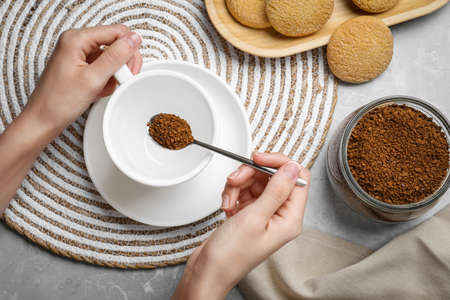 Woman pouring instant coffee into cup at light gray marble table, top view
