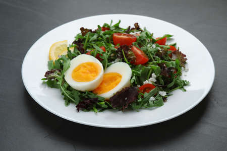 Delicious salad with boiled egg, arugula and tomatoes on black table, closeupの写真素材