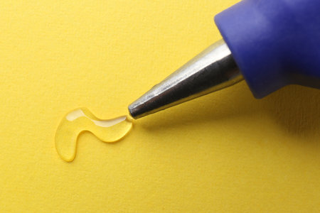 Melted glue dripping out of hot gun nozzle on yellow background, closeupの写真素材