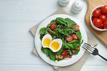 Delicious salad with boiled egg, bacon and tomatoes served on white wooden table, flat layの写真素材