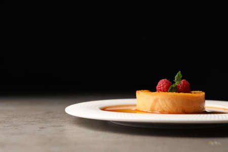 Delicious pudding with caramel and raspberries on gray table against black background. Space for textの写真素材