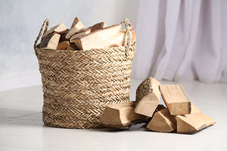 Wicker basket with cut firewood on white floor indoorsの写真素材