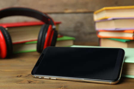Modern smartphone with blank screen and books on wooden table, closeup. space for designの写真素材