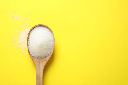 Granulated sugar in spoon on yellow background,top view. Space for textの写真素材