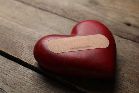 Heart with medical patch on wooden table, closeup. Relationship problems conceptの写真素材