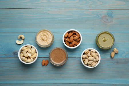Different types of delicious nut butters and ingredients on light blue wooden table, flat layの写真素材