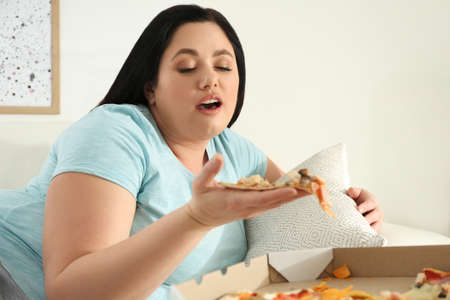 Lazy overweight woman eating pizza at homeの写真素材
