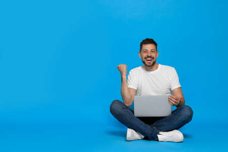 Happy man sitting with laptop on light blue background. Space for textの写真素材