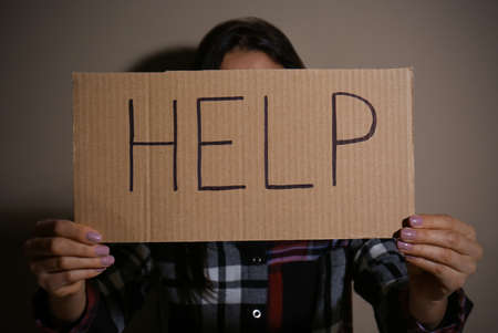 Young woman with sign HELP near beige wall. domestic violence concept