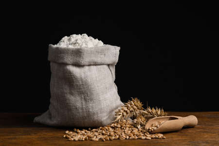 Wheat flour in sack bag, spikes and grains on wooden tableの写真素材