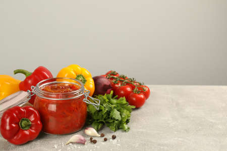 Glass jar of delicious canned lecho and fresh ingredients on light gray table. Space for textの写真素材