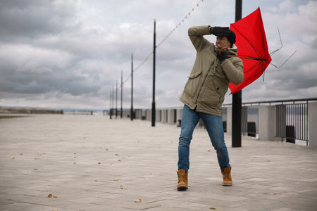 Man with red umbrella caught in the thick of wind outdoors