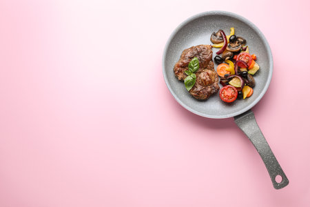 Tasty fried steak with vegetables in pan on pink background, top view. Space for textの写真素材