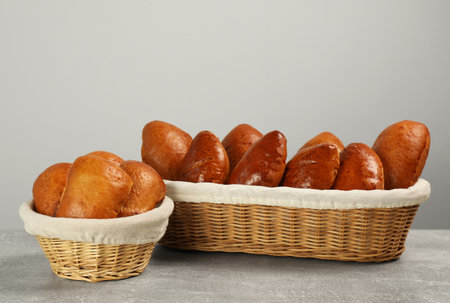 Delicious baked patties in wicker baskets on light gray table