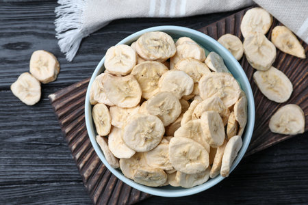Bowl and dried banana slices on black wooden table, top viewの写真素材