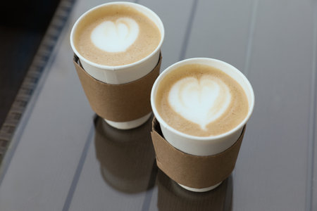 Paper takeaway cups of coffee with cardboard sleeves on glass table, above viewの写真素材