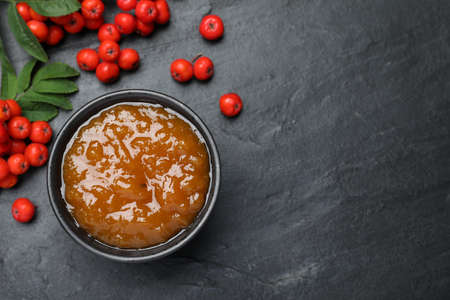 Delicious rowan jam in bowl and berries on dark table, flat lay. Space for textの写真素材