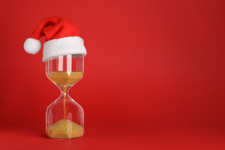 Hourglass and Santa hat on red background, space for text. christmas count downの写真素材